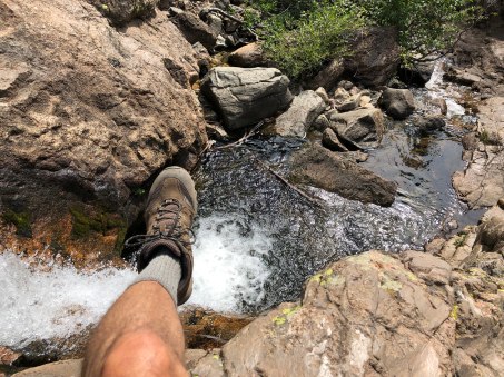 Michael taking a break and hanging his foot over the side of a rock looking down at the creek below